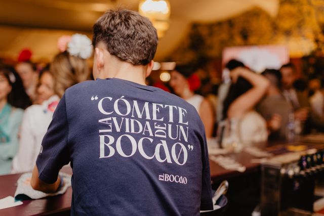 Camarero de espaldas con la camiseta «Cómete la vida de un Bocao» ante la carpa llena