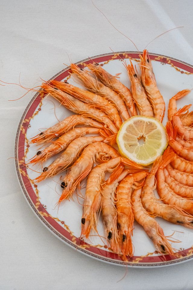 White prawns fanned out on a plate with lemon, seen from above