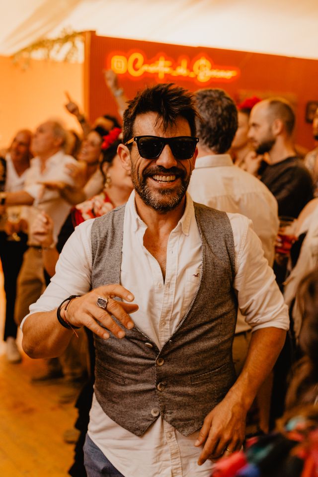 Invitado con gafas de sol bailando ante el neón de la caseta, evento de Hinojosa