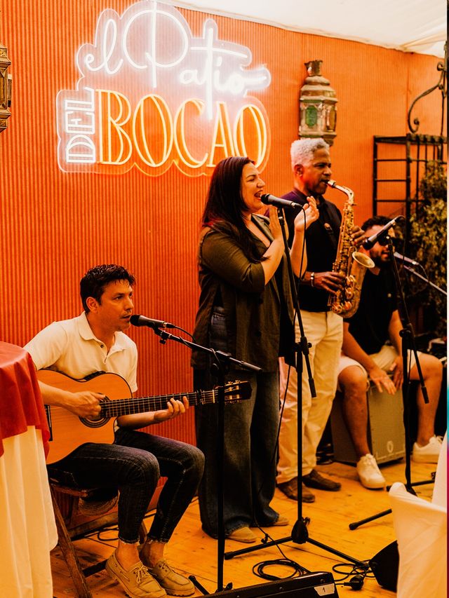 Grupo en directo con saxofón, guitarra y cajón ante el neón «El Patio del Bocao»