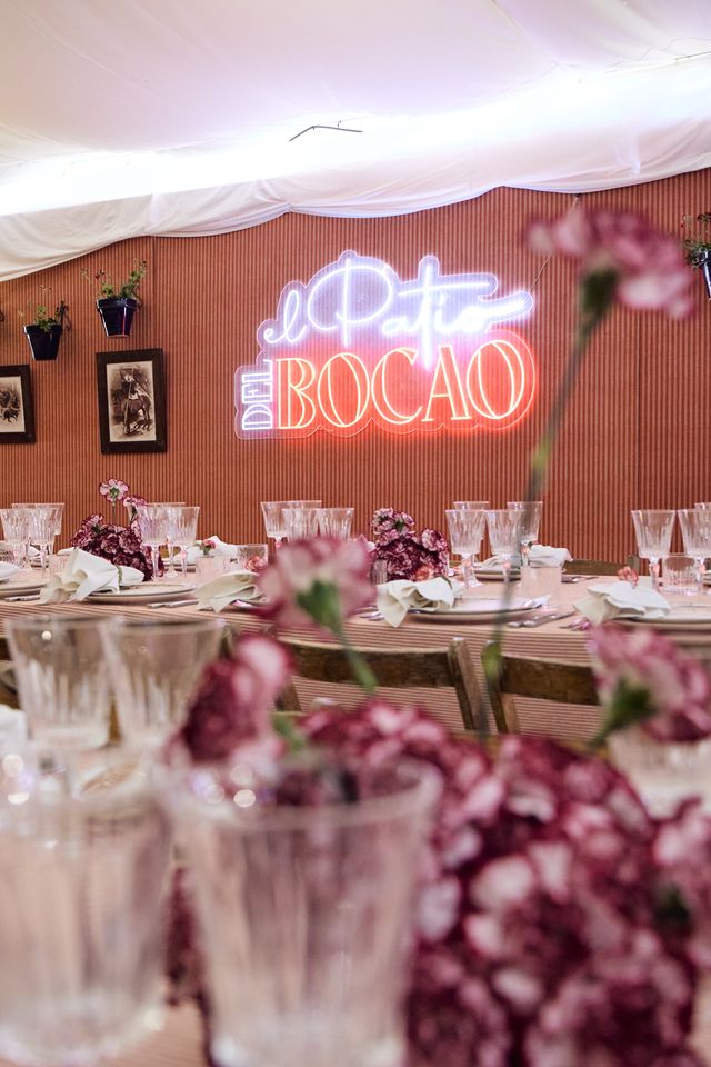 “El Patio del Bocao” neon above a laid table with carnations and glasses