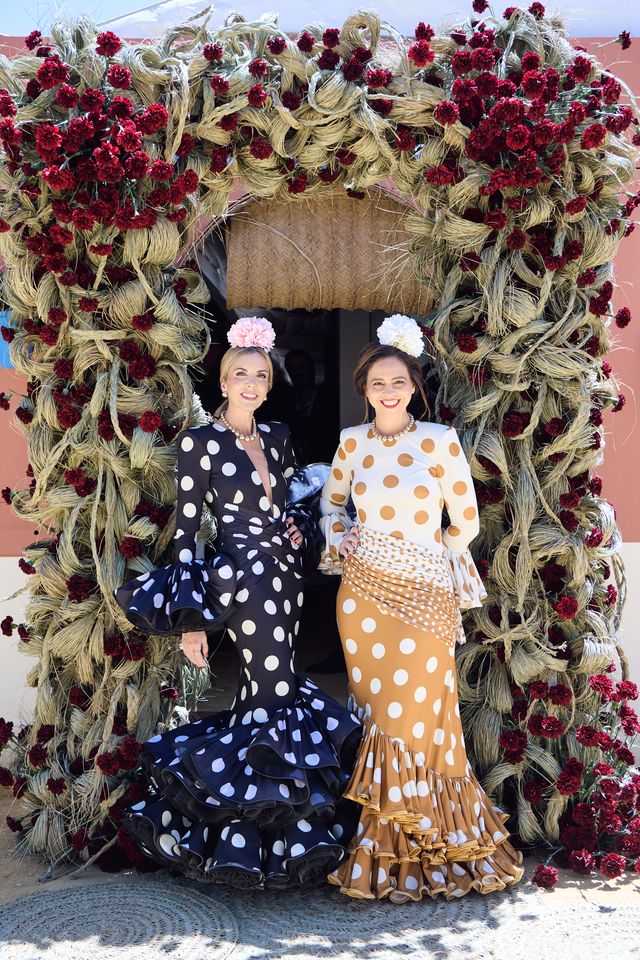 Dos invitadas con trajes de flamenca de lunares ante el arco floral del evento de Silbón